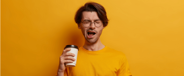 homem bocejando segurando copo de café na mão direita.