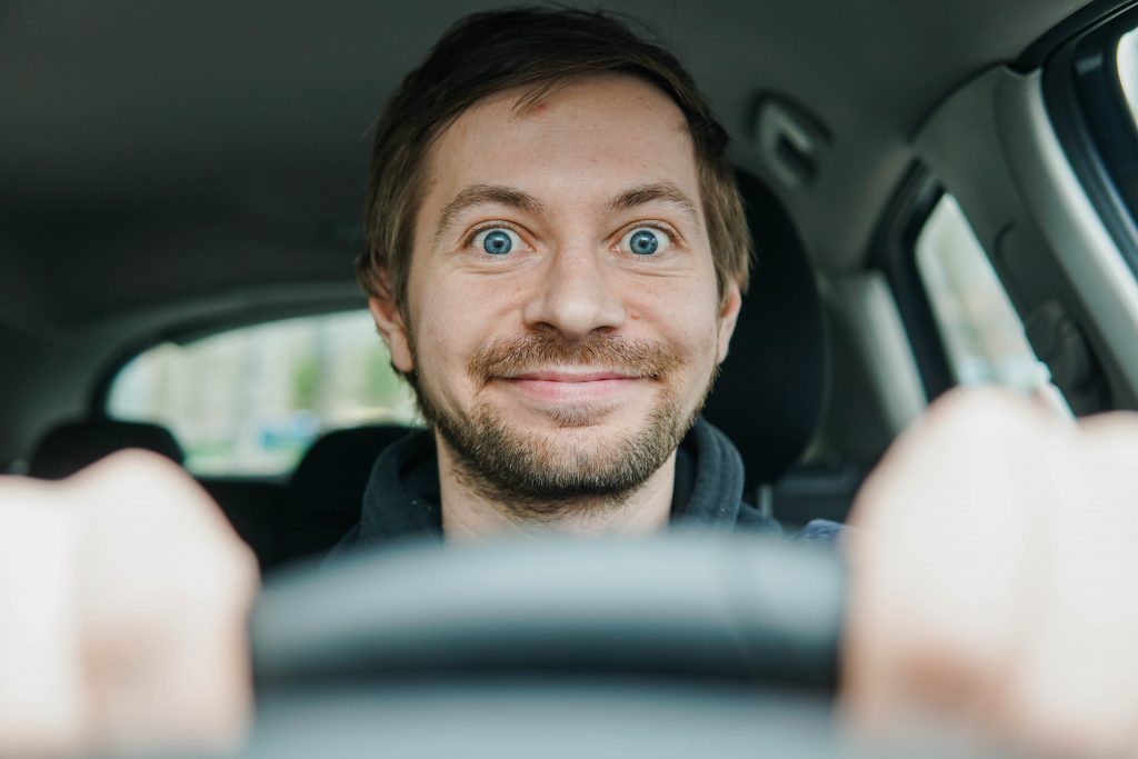 Foto de um motorista feliz e animado, atrás do volante do seu carro.
